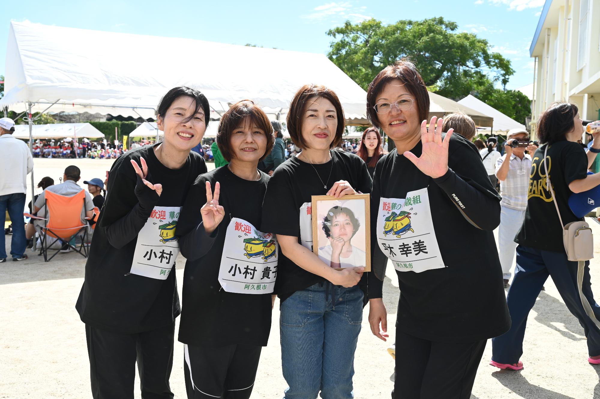 同級生の写真を持ちながら笑顔で撮影をする女性4人組の写真