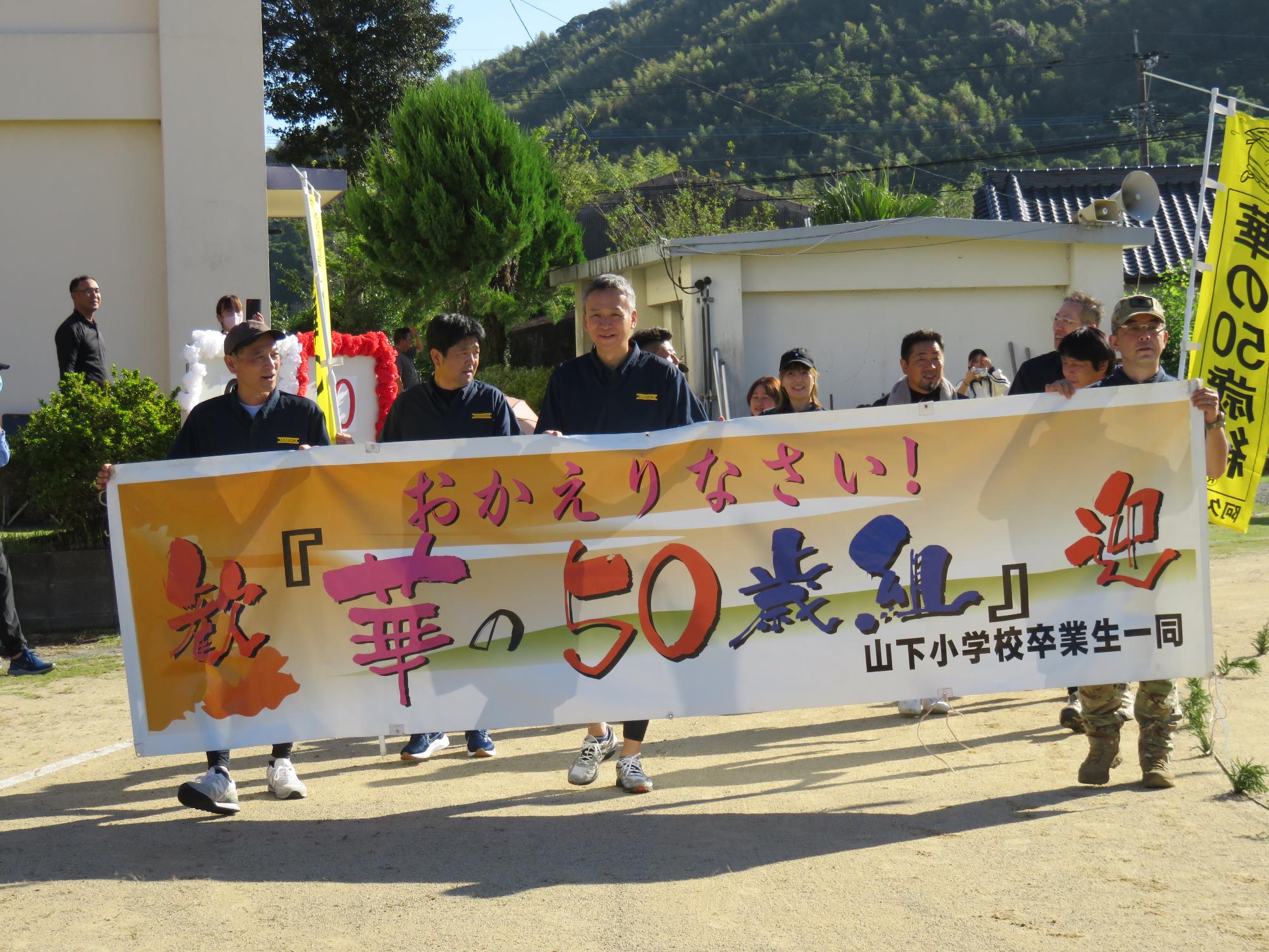 山下小華の50歳組の横断幕を持って歩く参加者の写真その1