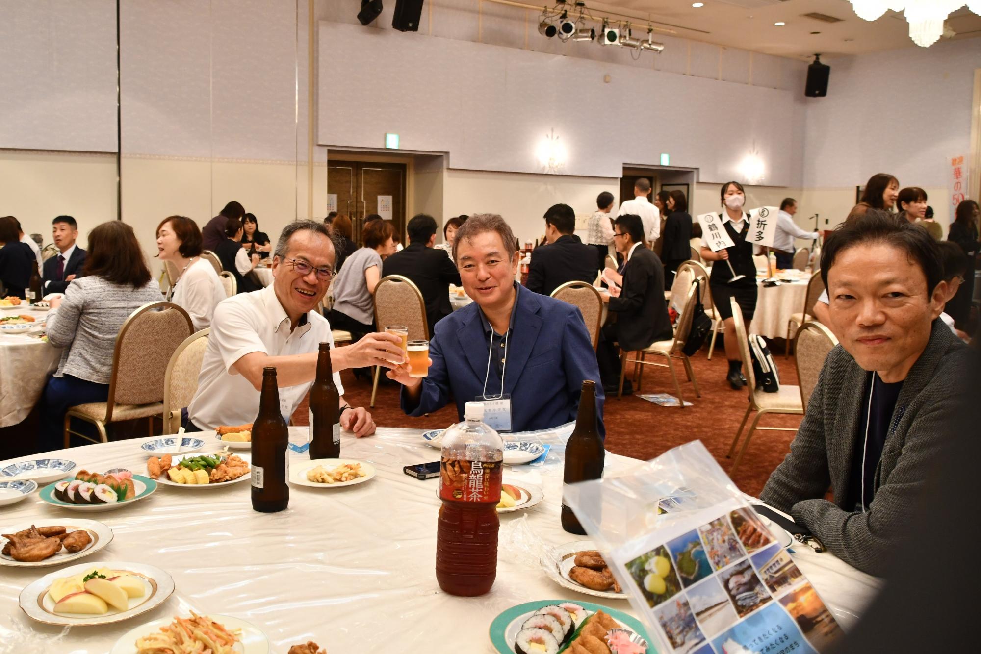 阿久根小出身の参加者たちの写真（テーブルを囲み乾杯をしている3人の男性）