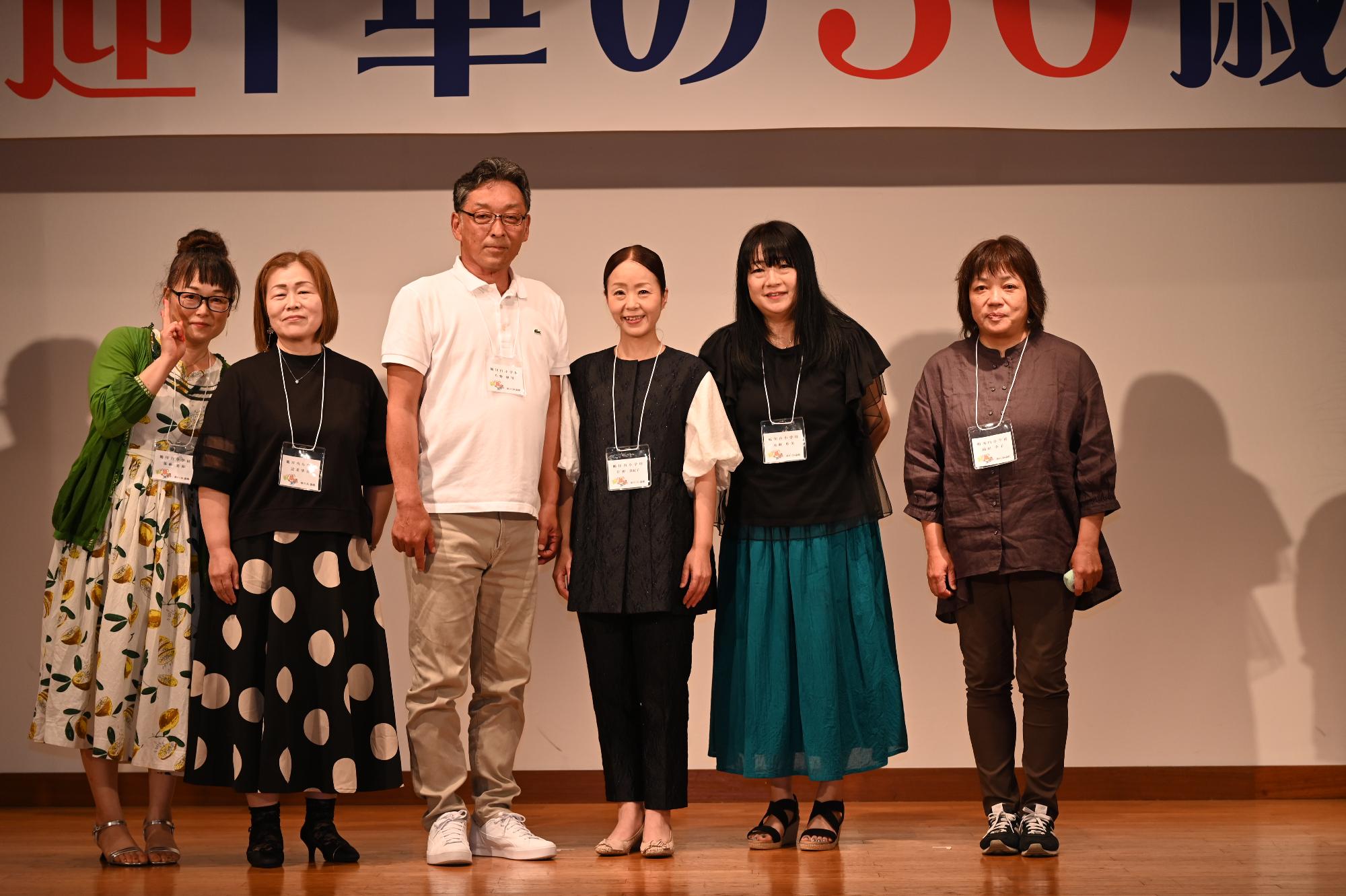 「歓迎 華の50歳組」と書かれた横断幕の前に並ぶ参加者たちの集合写真（鶴川内小）