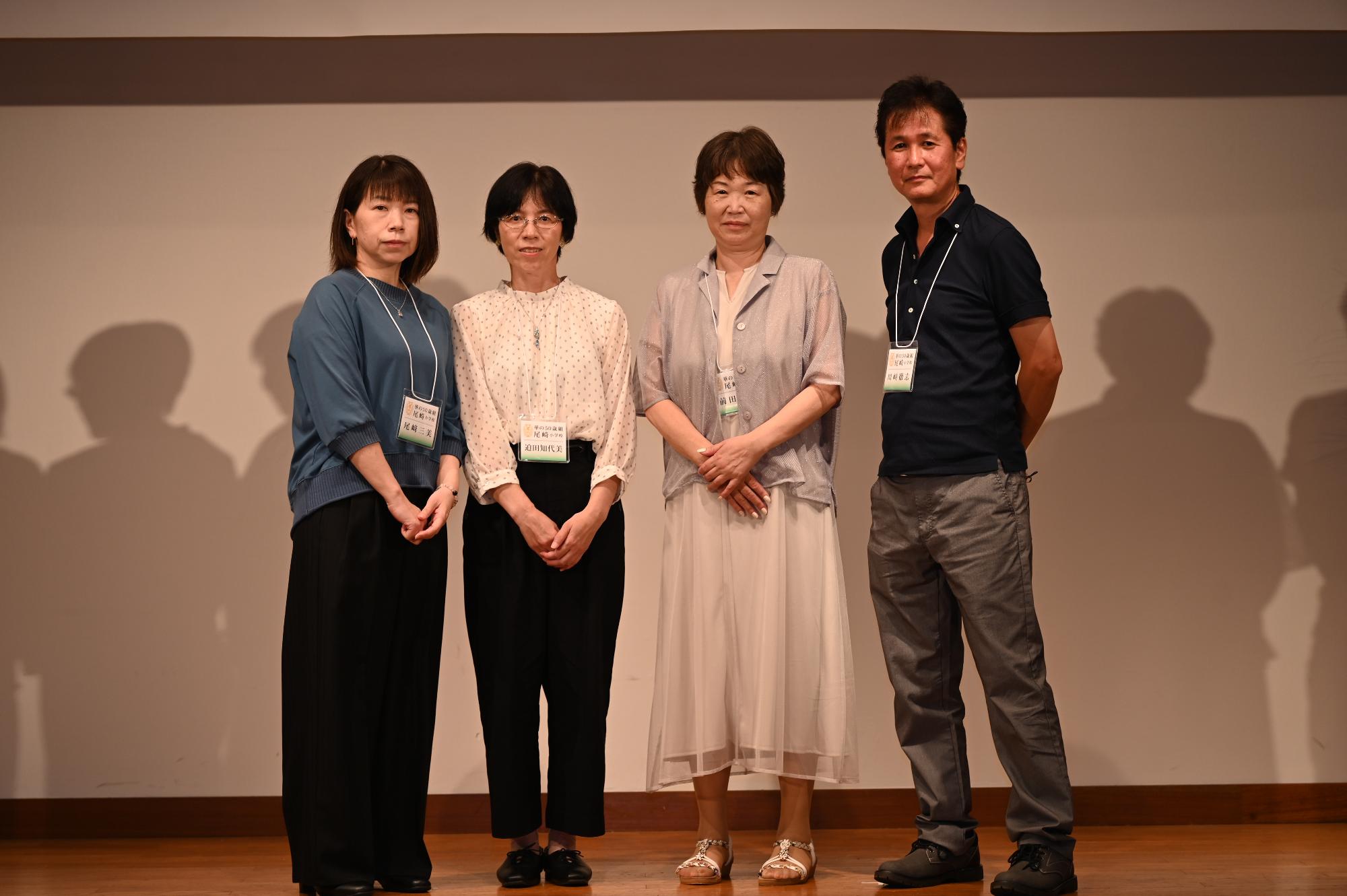 「歓迎 華の50歳組」と書かれた横断幕の前に並ぶ参加者たちの集合写真（尾崎小）