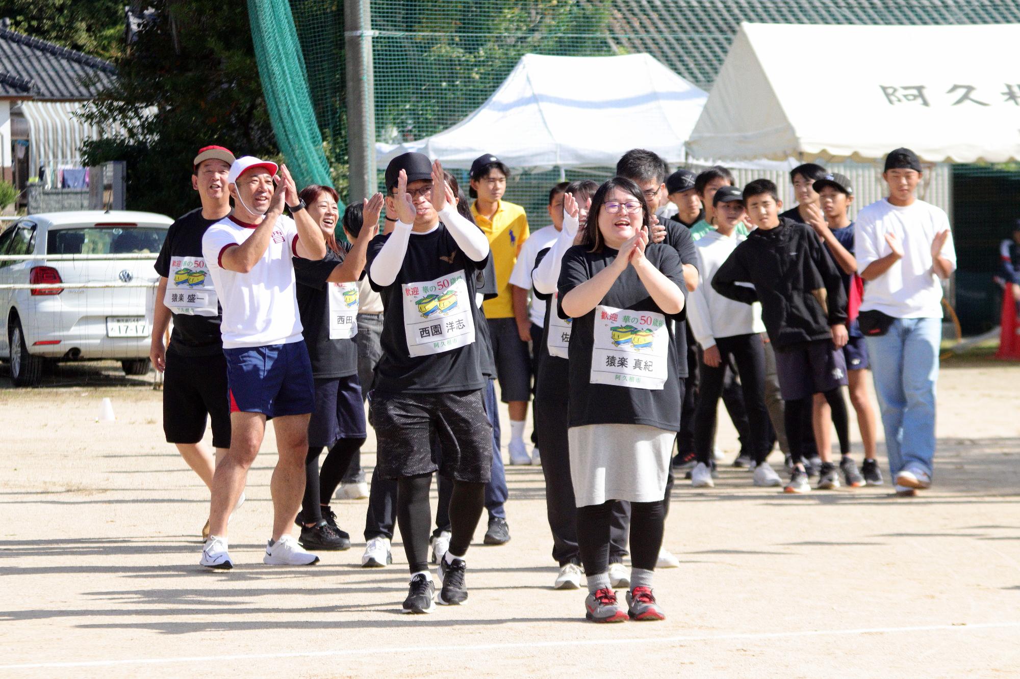手拍子をしながら入場行進をする西目小学校華の50歳組の参加者の写真