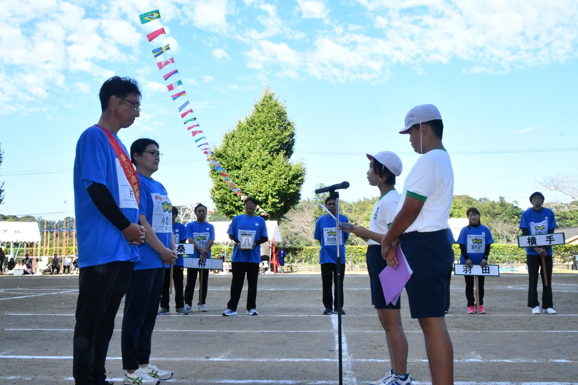 華の50歳組参加者へあいさつをする小学生の写真