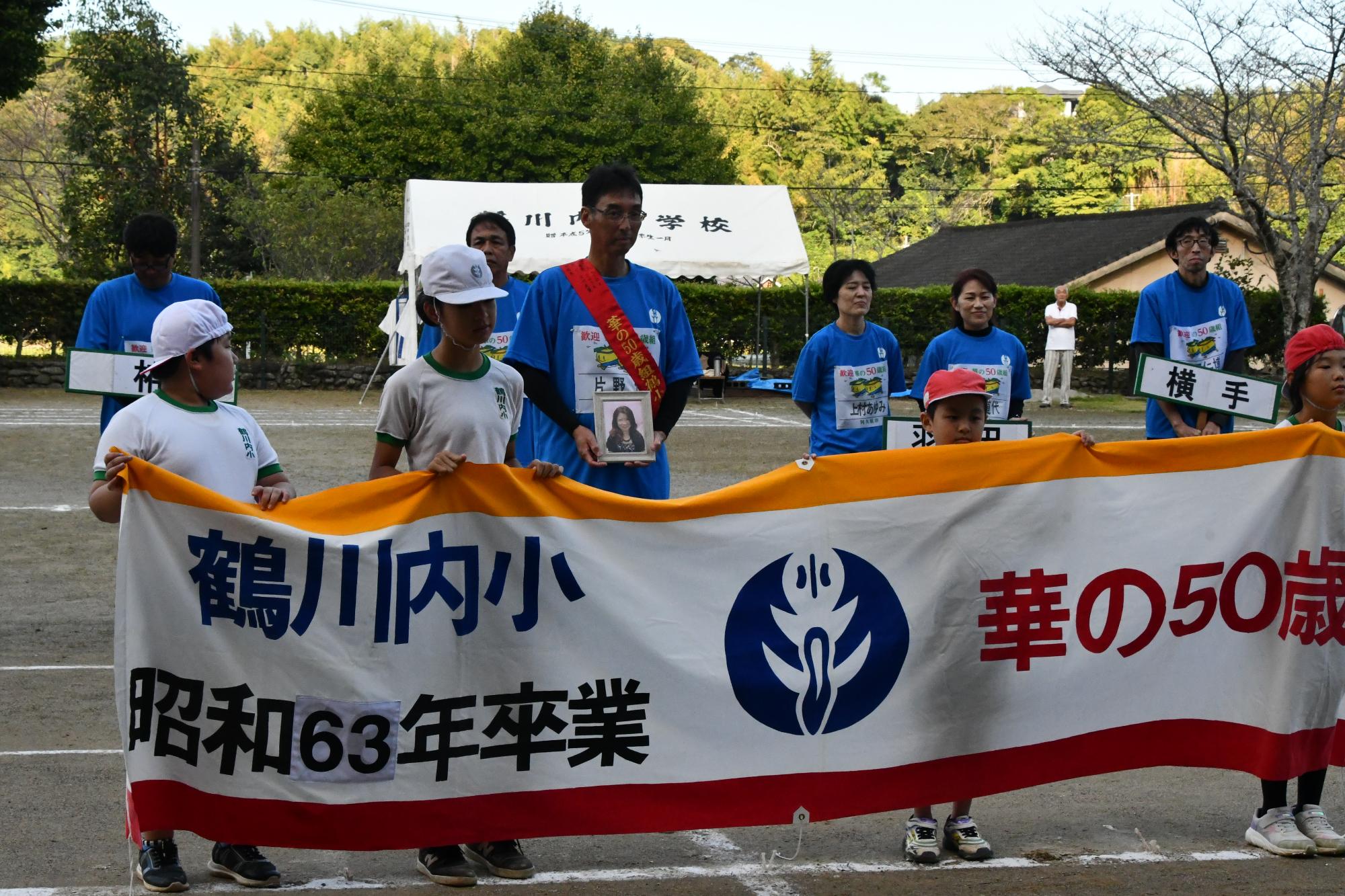 小学生が横断幕を持つ後ろに整列する参加者の写真
