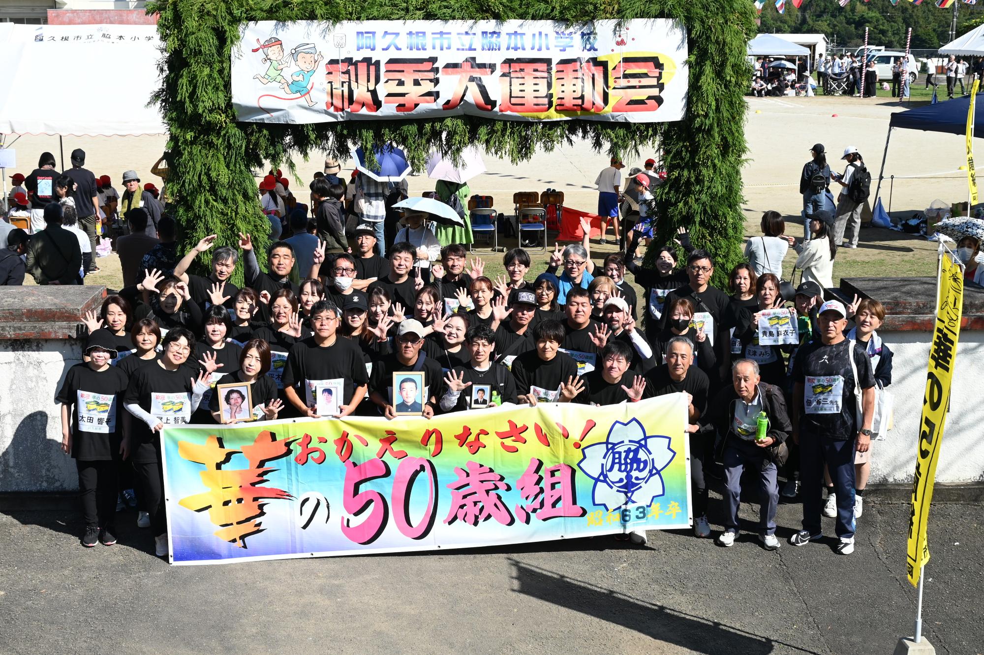 校門前で華の50歳組の横断幕を持ちながら写真を撮る参加者の写真