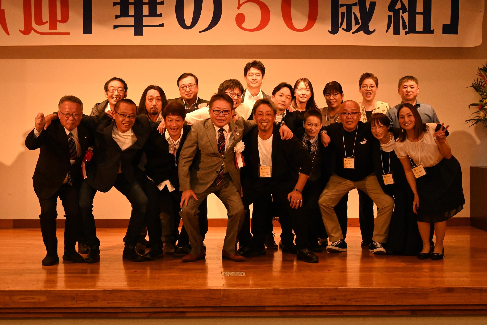 「歓迎 華の50歳組」と書かれた横断幕の前に並ぶ参加者たちの集合写真（折多小）