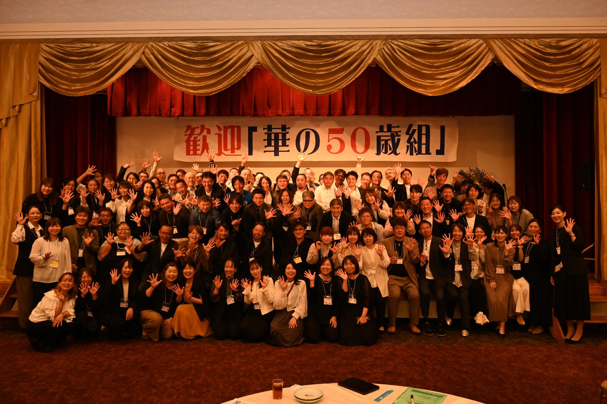 「歓迎 華の50歳組」と書かれた横断幕の前に並ぶ参加者たちの集合写真（その他の高校出身）