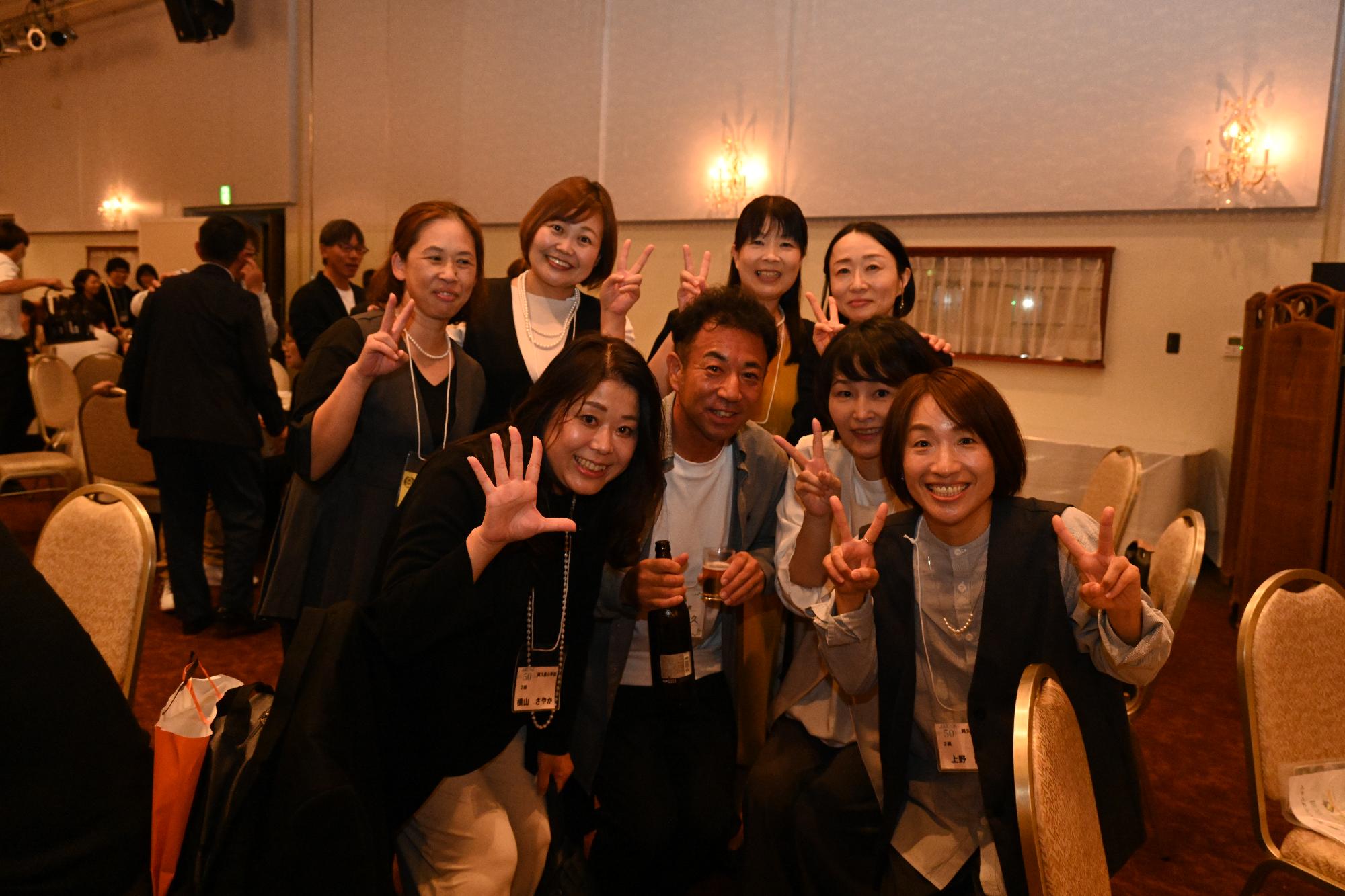 テーブルの近くでピースをする男女8人の写真