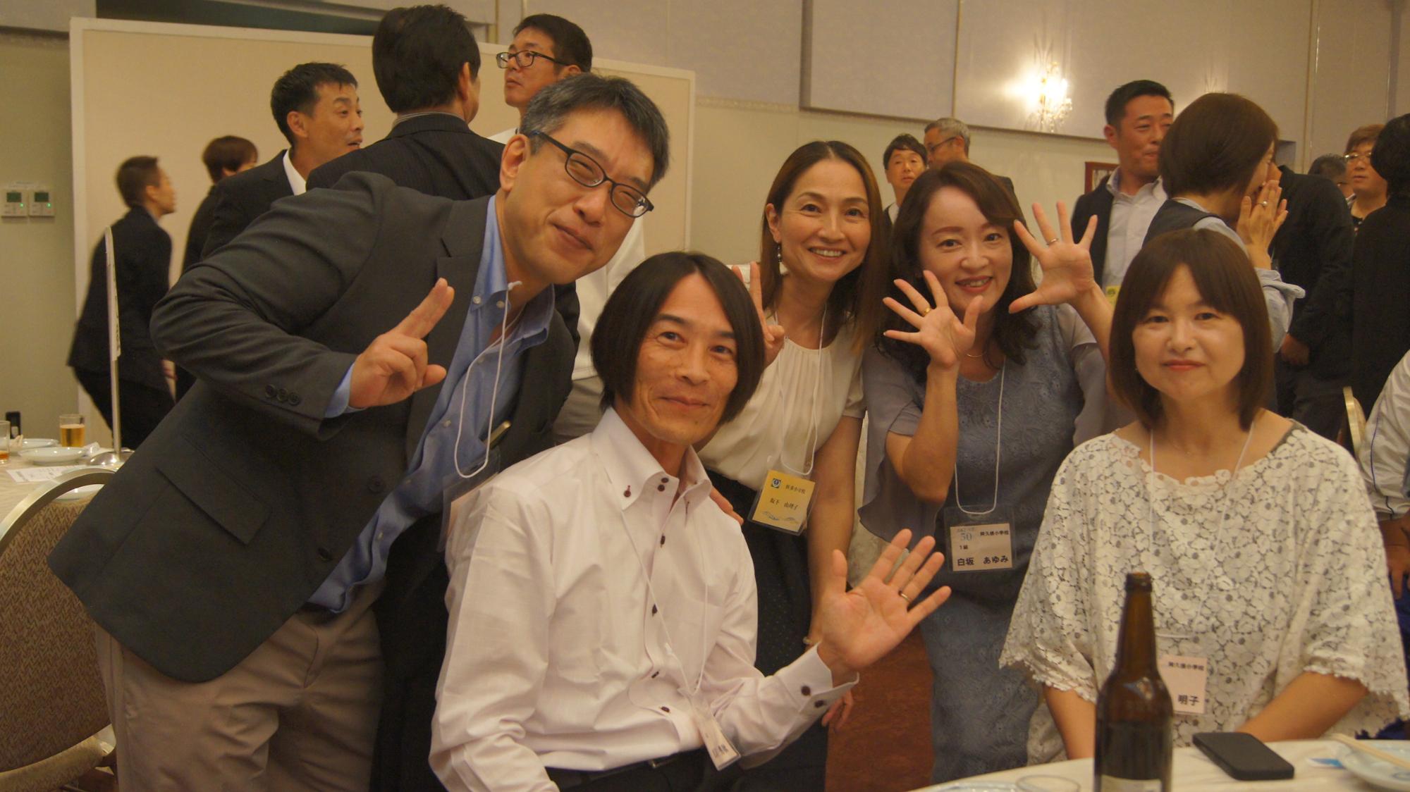 テーブルでポーズをとる阿久根小出身の男女5人の写真