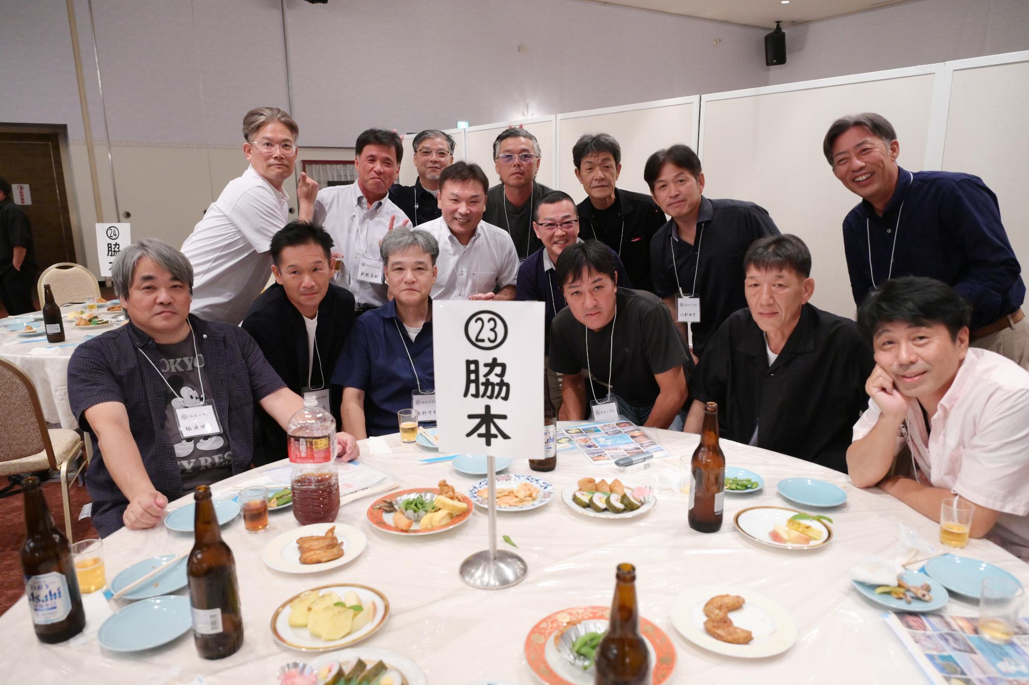 脇本小出身の参加者たちの写真（テーブルを囲む15人の男性）