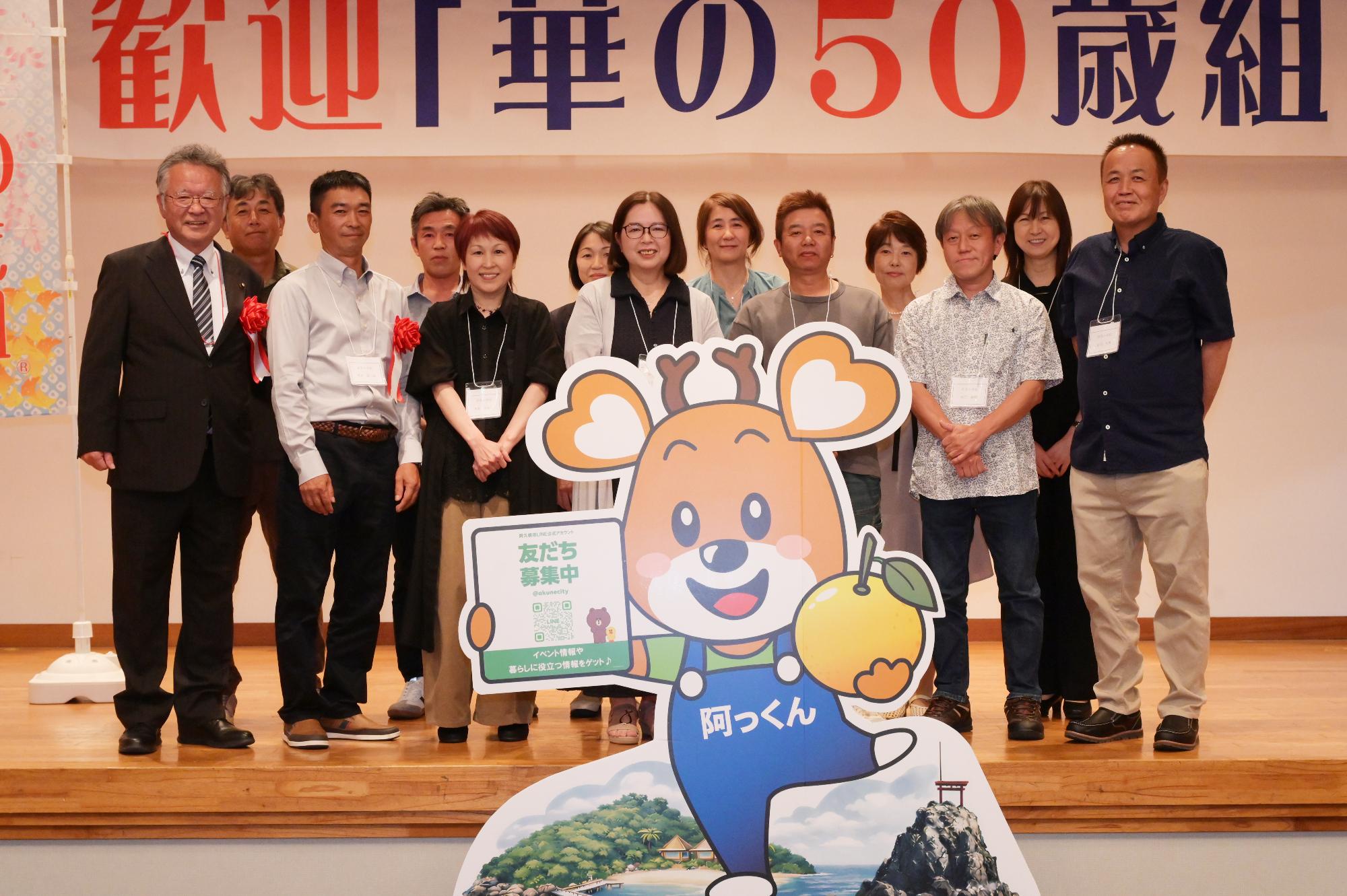 「歓迎 華の50歳組」と書かれた横断幕の前に並ぶ参加者たちの集合写真（折多小）