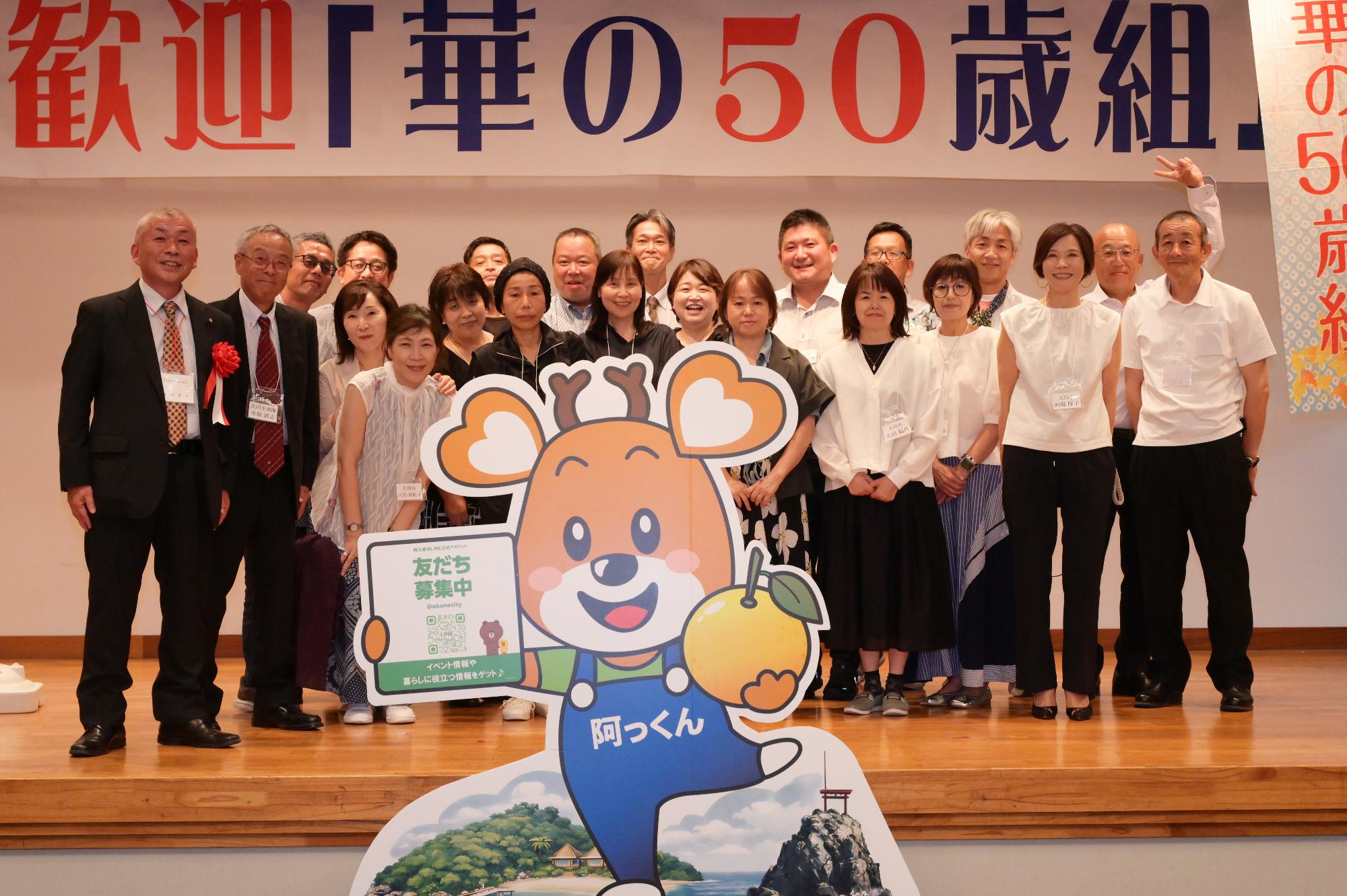 「歓迎 華の50歳組」と書かれた横断幕の前に並ぶ参加者たちの集合写真（大川小）