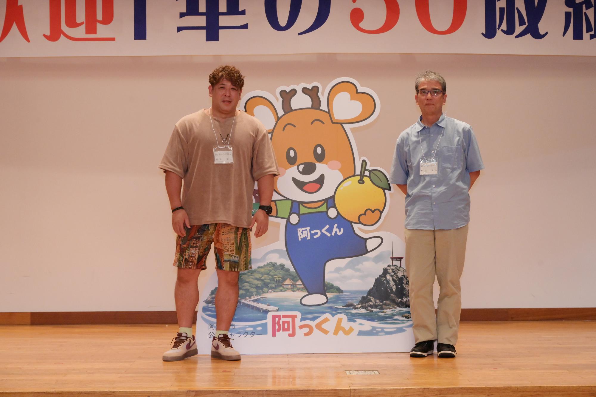 「歓迎 華の50歳組」と書かれた横断幕の前に並ぶ参加者たちの集合写真（鶴川内小）