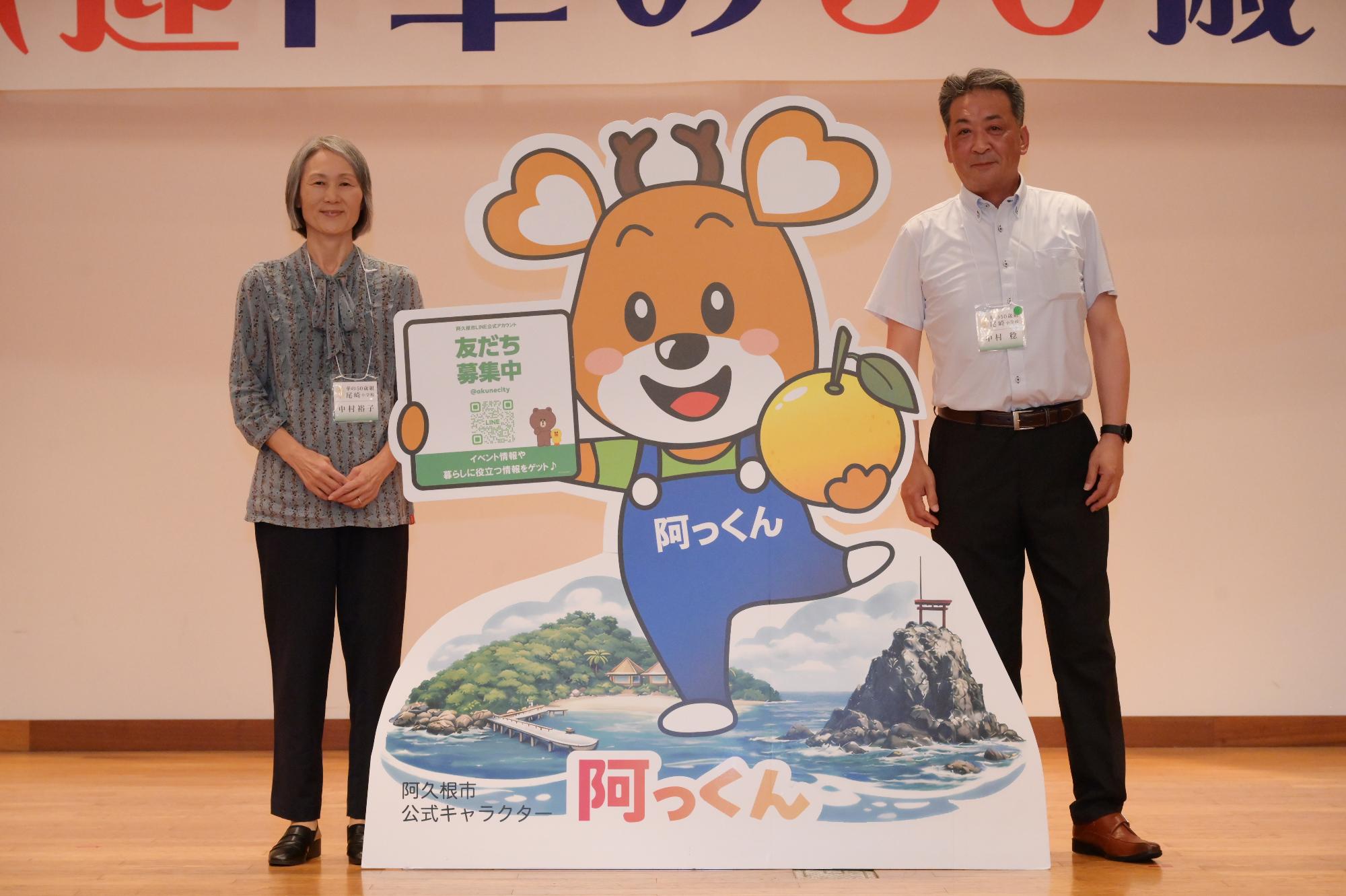 「歓迎 華の50歳組」と書かれた横断幕の前に並ぶ参加者たちの集合写真（尾崎小）