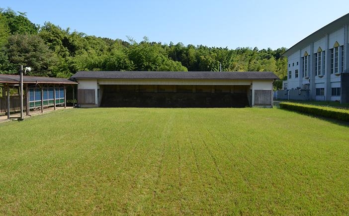 緑豊かな芝生が広がる奥に屋根のかかった横長な的場がある弓道場の写真