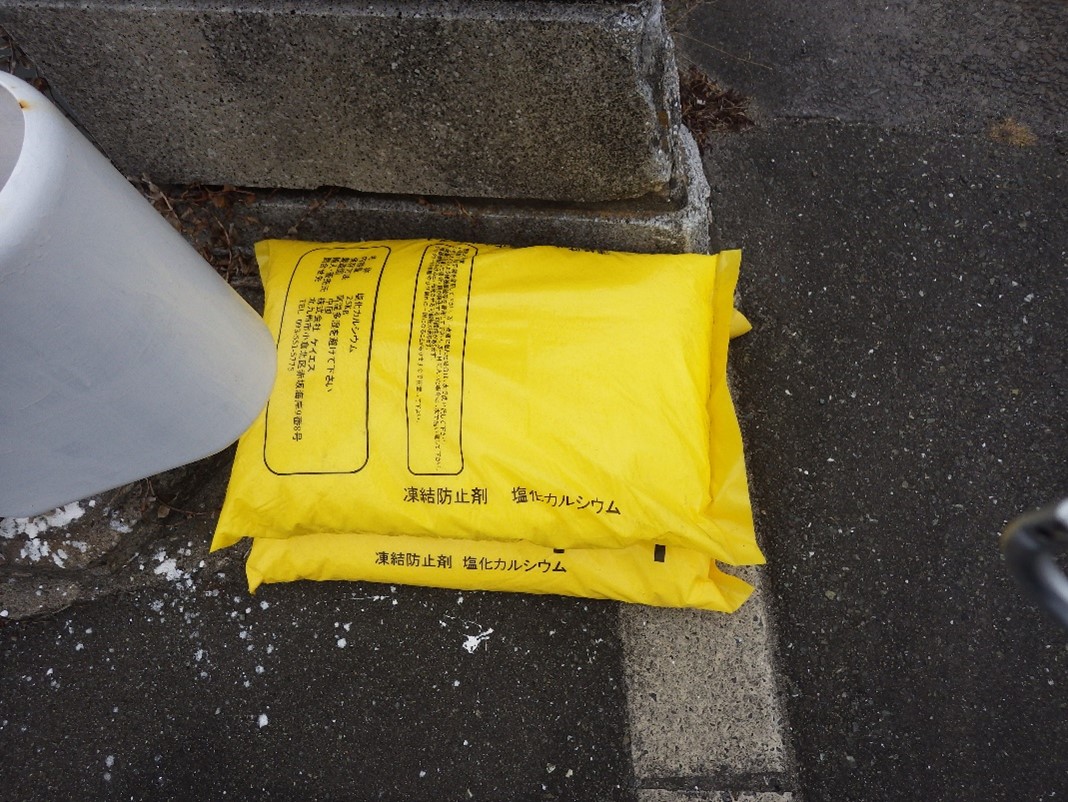 凍結防止剤 塩化カルシウムの入った黄色い袋が道路上に2つ積み重ねられている写真