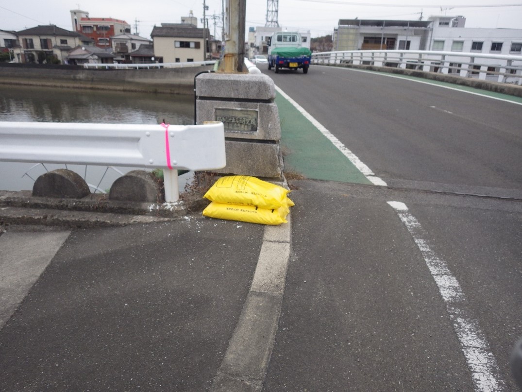 凍結防止剤 塩化カルシウムの入った黄色い袋が道路上に2つ積み重ねられている写真（引きの写真）